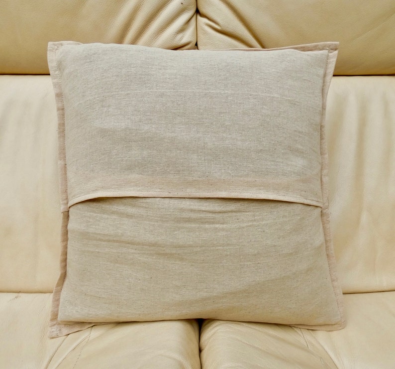 Puede incluir: Una almohada rectangular lisa de color blanco roto con una cremallera en la parte posterior. La almohada est&aacute; hecha de una tela suave y natural y est&aacute; sentada en un sof&aacute; de cuero marr&oacute;n claro.