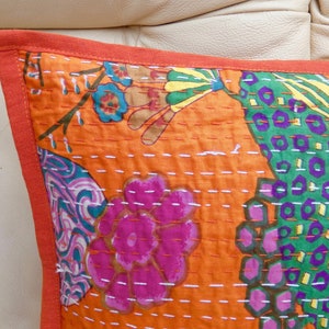 Peut inclure: Gros plan d'un coussin orange d&eacute;coratif avec un motif floral rose, vert et bleu. Le coussin a une bordure orange unie et est cousu avec du fil blanc. Il s'agit probablement d'un article de d&eacute;coration int&eacute;rieure.