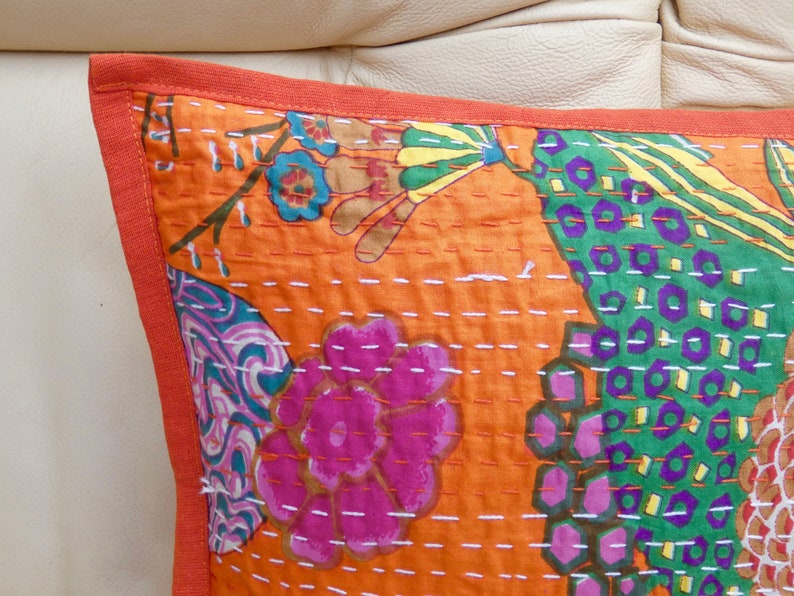 Peut inclure: Gros plan d'un coussin orange d&eacute;coratif avec un motif floral rose, vert et bleu. Le coussin a une bordure orange unie et est cousu avec du fil blanc. Il s'agit probablement d'un article de d&eacute;coration int&eacute;rieure.