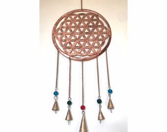 Op de afbeelding: Een koperkleurige metalen wanddecoratie met een geometrisch bloem des levens-ontwerp. Het cirkelvormige stuk heeft hangende kettingen met kleurrijke kralen en kleine belaccenten. Geschikt voor woondecoratie.
