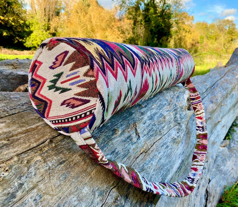 Pu&ograve; includere: Un bolster da yoga cilindrico con una fodera in tessuto colorato e fantasia. Il design presenta un mix di motivi geometrici e tribali nei toni del rosso, blu, verde e marrone. Ha un manico in tessuto abbinato.