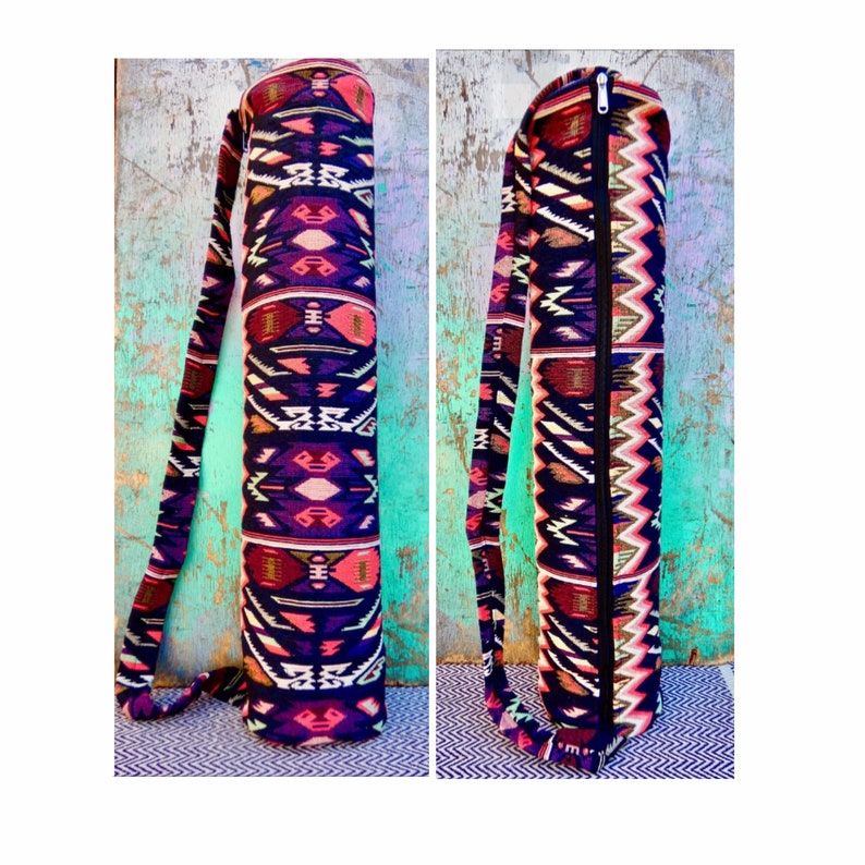 May include: A yoga mat carrier with a black zipper and a colorful geometric pattern in shades of pink, red, white, and blue. The carrier has a long strap for carrying over the shoulder.