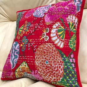 K&ouml;nnte beinhalten: Rotes und rosa Kissen mit floralem Muster und wei&szlig;en N&auml;hten. Das Kissen hat einen gr&uuml;nen Rand.