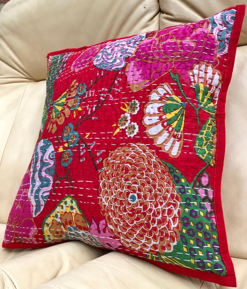 K&ouml;nnte beinhalten: Rotes und rosa Kissen mit floralem Muster und wei&szlig;en N&auml;hten. Das Kissen hat einen gr&uuml;nen Rand.