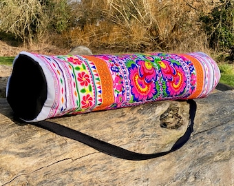 May include: A white yoga mat bag with a colorful floral pattern and a black strap. The bag is made of fabric and has a zipper closure.