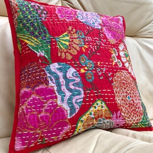 K&ouml;nnte beinhalten: Roter Kissenbezug aus Baumwolle mit einem floralen Muster mit rosa, gr&uuml;nen, blauen und gelben Blumen. Der Kissenbezug ist mit wei&szlig;em Garn gesteppt.