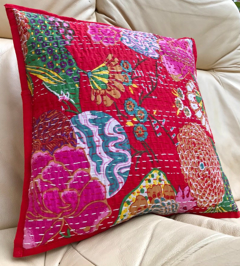 K&ouml;nnte beinhalten: Roter Kissenbezug aus Baumwolle mit einem floralen Muster mit rosa, gr&uuml;nen, blauen und gelben Blumen. Der Kissenbezug ist mit wei&szlig;em Garn gesteppt.