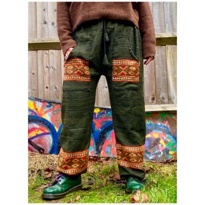 May include: Green trousers with a colourful geometric pattern on the legs. The trousers have a drawstring waist and pockets.