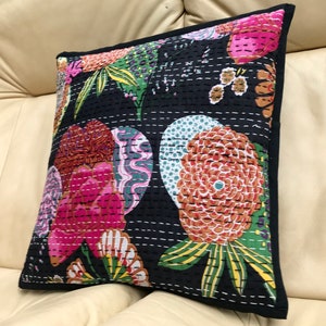 May include: Black cotton pillow cover with a floral pattern in shades of pink, orange, green, and white. The pillow cover is quilted with a black thread and has a black border.