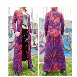 May include: A long, purple and red tie-dye cardigan with long sleeves and pockets. The cardigan is open at the front and has a relaxed fit.