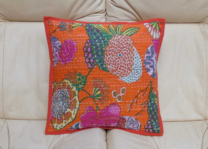 Peut inclure: Coussin carr&eacute; orange avec un motif floral rose, vert et bleu. Le coussin a une bordure rouge et est fait d'un tissu matelass&eacute;. Le motif comprend des fleurs et des fruits stylis&eacute;s.