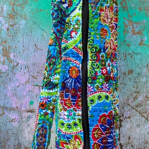 May include: A patterned yoga mat bag in blue, green, red, and orange. The bag features a black zip and a matching strap. The bag is made of a quilted fabric with a floral design. The bag is designed to carry a yoga mat.