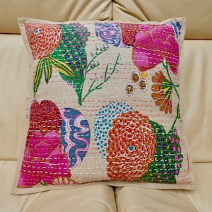 Puede incluir: Una almohada cuadrada con fondo blanco y un estampado floral colorido. La almohada presenta flores rosas, naranjas, verdes y azules con intrincados detalles de costura.