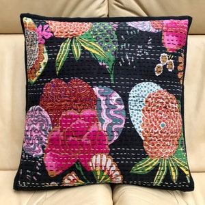May include: Black cotton cushion cover with a floral pattern in shades of pink, orange, green, and white. The cushion cover has a quilted design and a black border.