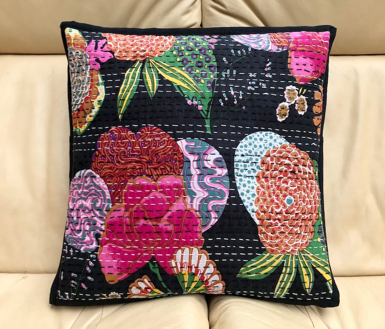 May include: Black cotton cushion cover with a floral pattern in shades of pink, orange, green, and white. The cushion cover has a quilted design and a black border.