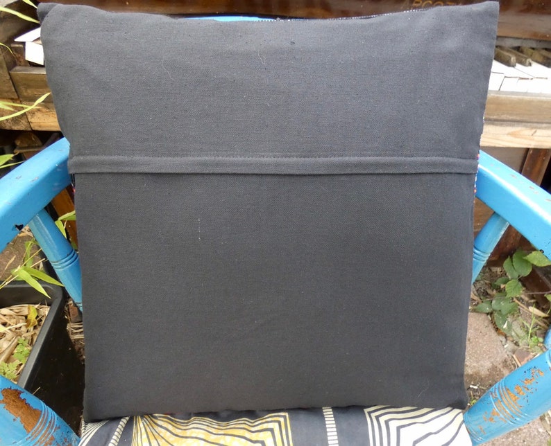 Puede incluir: Coj&iacute;n cuadrado negro con una costura cosida en el medio. El coj&iacute;n est&aacute; sobre una silla azul con un asiento estampado. La parte trasera del coj&iacute;n es de tela negra lisa.
