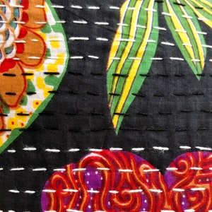 May include: Close-up of a black fabric with white stitching. The fabric has a colorful floral pattern with red, orange, yellow, green, and purple hues. The stitching creates a quilted effect.