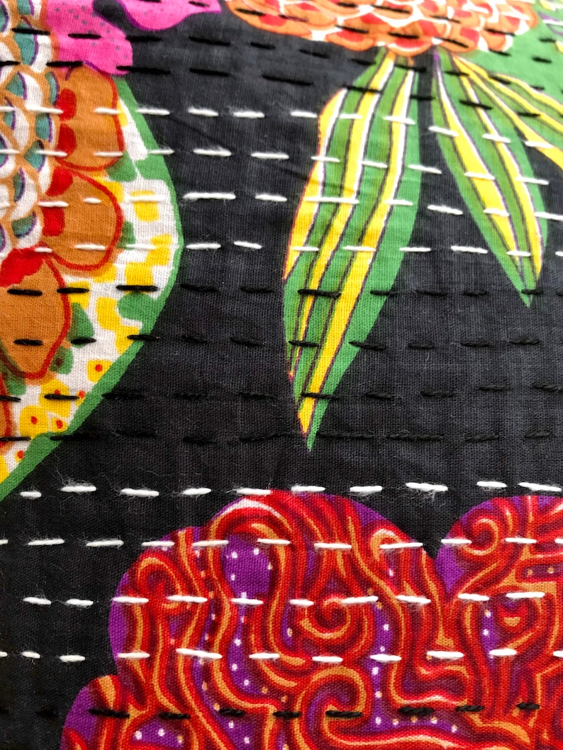 May include: Close-up of a black fabric with white stitching. The fabric has a colorful floral pattern with red, orange, yellow, green, and purple hues. The stitching creates a quilted effect.