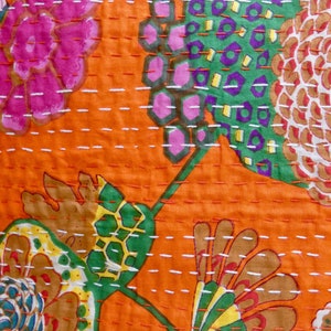 Peut inclure: Gros plan sur un tissu orange vif avec un motif floral. Le motif pr&eacute;sente de grandes fleurs dans des tons de rose, vert, marron et jaune, avec des coutures blanches. Le tissu a un aspect textur&eacute;, sugg&eacute;rant une courtepointe ou un textile.