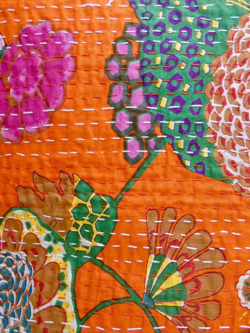 Peut inclure: Gros plan sur un tissu orange vif avec un motif floral. Le motif pr&eacute;sente de grandes fleurs dans des tons de rose, vert, marron et jaune, avec des coutures blanches. Le tissu a un aspect textur&eacute;, sugg&eacute;rant une courtepointe ou un textile.