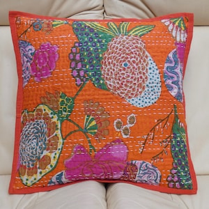 Peut inclure: Coussin carr&eacute; orange avec un motif floral rose, vert et bleu. Il pr&eacute;sente une bordure rouge et des coutures blanches. Le coussin est probablement en tissu.