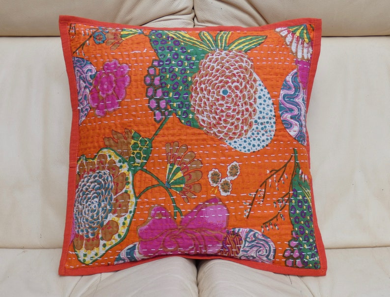 Peut inclure: Coussin carr&eacute; orange avec un motif floral rose, vert et bleu. Il pr&eacute;sente une bordure rouge et des coutures blanches. Le coussin est probablement en tissu.
