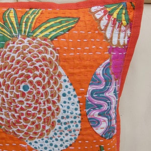 Peut inclure: Gros plan sur un coussin d&eacute;coratif orange avec un motif d'ananas et floral. Le coussin pr&eacute;sente un fond orange vif avec des coutures blanches et une bordure rouge. L'ananas a un motif marron, blanc et rouge.