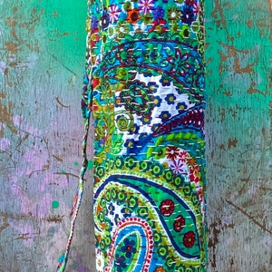 May include: A cylindrical yoga mat bag with a vibrant paisley design in blue, green, red, and white. The bag features a matching strap and is constructed from stitched fabric.