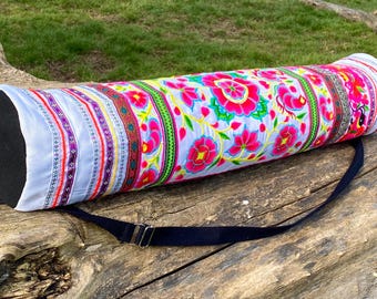 May include: A white yoga mat bag with a colorful floral pattern and a black carrying strap. The bag has a black zipper and a black handle.