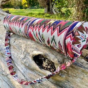 Pu&ograve; includere: Una borsa cilindrica per tappetino da yoga con una fodera in tessuto fantasia. Il design presenta un motivo a zig-zag ripetuto in rosso, verde, blu e marrone su sfondo crema. &Egrave; attaccata una cinghia abbinata per il trasporto.