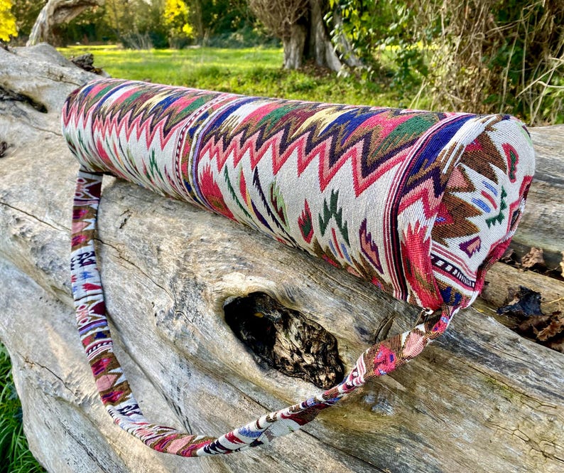 Pu&ograve; includere: Una borsa cilindrica per tappetino da yoga con una fodera in tessuto fantasia. Il design presenta un motivo a zig-zag ripetuto in rosso, verde, blu e marrone su sfondo crema. &Egrave; attaccata una cinghia abbinata per il trasporto.
