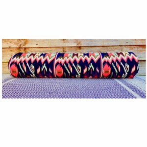 May include: A long, cylindrical pillow with a colorful geometric pattern in shades of pink, blue, and white. The pillow is made of a soft, woven fabric and has a slightly textured surface.