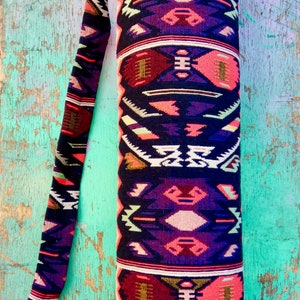 May include: A black yoga mat bag with a colorful geometric pattern in shades of pink, red, purple, white, and gold. The bag has a long strap for carrying over the shoulder.