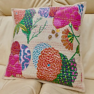 Puede incluir: Una funda de coj&iacute;n de color crema con un patr&oacute;n floral. Las flores son rosas, naranjas, verdes y azules. La funda de coj&iacute;n est&aacute; acolchada y tiene un brillo sutil.