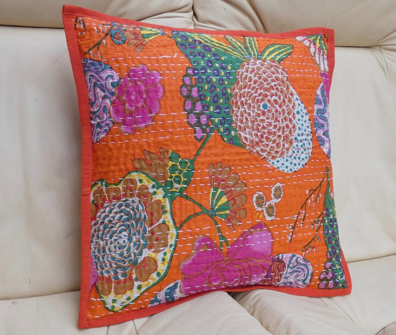 Peut inclure: Coussin carr&eacute; orange avec un motif floral rose, vert et bleu. Le coussin a une bordure rouge et des coutures blanches. Le coussin mesure environ 45 cm de c&ocirc;t&eacute;.