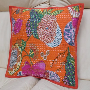 Peut inclure: Coussin carr&eacute; orange avec un motif floral vibrant en rose, vert et bleu. Le coussin a une bordure rouge et des coutures blanches. Il est pos&eacute; sur une surface blanche.