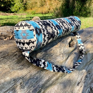May include: A blue and black yoga mat carrier with a geometric pattern. The carrier has a long strap for carrying over the shoulder.