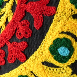 Puede incluir: Primer plano de una tela negra con vibrantes patrones florales bordados. El bordado presenta hilos rojos, amarillos y verdes, creando un dise&ntilde;o decorativo texturizado. El dise&ntilde;o incluye hojas estilizadas y formas de flores.