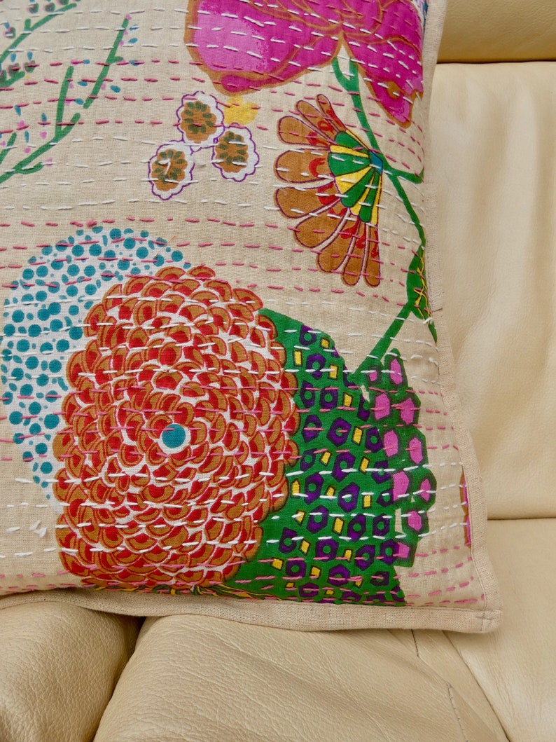 Puede incluir: Una funda de coj&iacute;n de algod&oacute;n beige con un patr&oacute;n floral. El patr&oacute;n presenta flores rosas, rojas, naranjas, verdes, azules y amarillas. La funda de coj&iacute;n est&aacute; acolchada con hilo blanco.