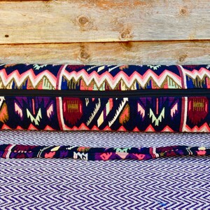 May include: A black yoga mat bag with a colorful geometric pattern and a zipper closure. The bag has a long strap for carrying over the shoulder.