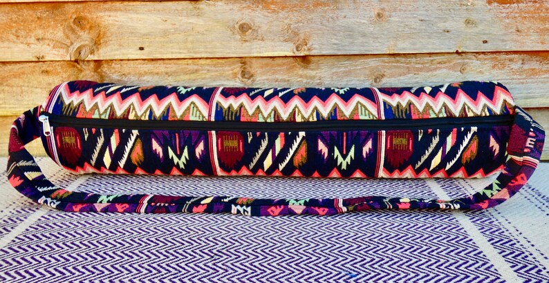May include: A black yoga mat bag with a colorful geometric pattern and a zipper closure. The bag has a long strap for carrying over the shoulder.