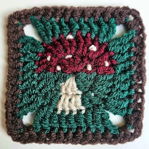 This image shows a singular crocheted square with a toadstool motif, shown on a plain white background. The toadstool is red and white, with white dots. It has a deep green surround and a brown border.