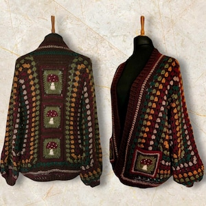 May include: A brown crocheted cardigan with a colourful geometric pattern and mushroom motifs. The cardigan has a V-neck and long sleeves.
