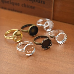 May include: Six silver and gold-toned rings with clear glass or resin insets. The rings are designed to hold a small charm or other embellishment. The insets are 12mm in diameter.