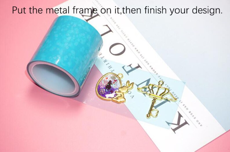 May include: A roll of turquoise blue epoxy resin tape, a gold heart-shaped pendant with a rabbit and a gold key with a crown on top. The text "Put the metal frame on it, then finish your design." is visible in the image.
