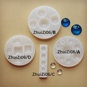 May include: Four silicone molds for making resin crafts. The molds are labeled "ZhuiZi06/A", "ZhuiZi06/B", "ZhuiZi06/C", and "ZhuiZi06/D". The molds are white and feature different shapes, including circles, squares, and rectangles. There are also two blue glass cabochons and two clear glass cabochons.