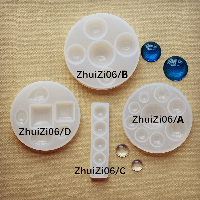 May include: Four silicone molds for making resin crafts. The molds are labeled "ZhuiZi06/A", "ZhuiZi06/B", "ZhuiZi06/C", and "ZhuiZi06/D". The molds are white and feature different shapes, including circles, squares, and rectangles. There are also two blue glass cabochons and two clear glass cabochons.