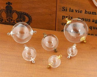 May include: Six clear glass spheres with silver and gold metal loops. The spheres are of varying sizes and are arranged on a wooden surface.