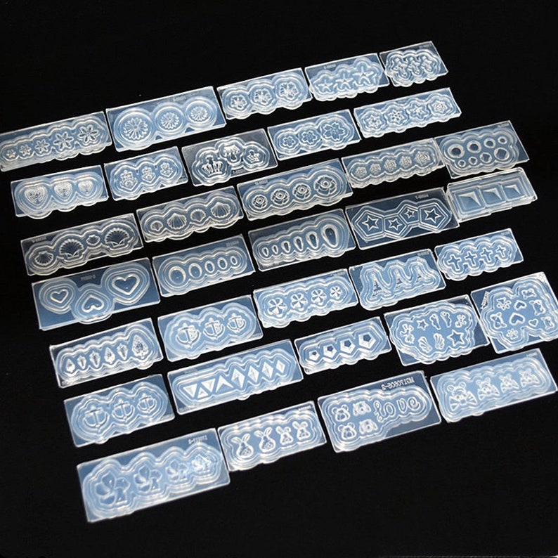 May include: A set of 25 clear silicone molds for nail art. The molds feature a variety of designs, including flowers, hearts, stars, and geometric shapes.