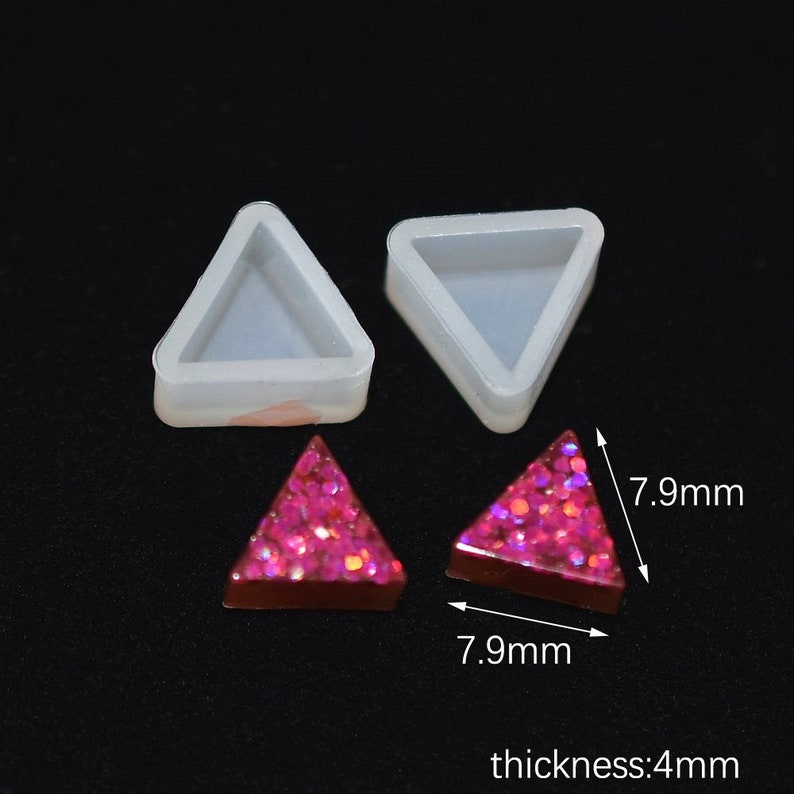 以下が含まれることがあります： 三角形の樹脂製イヤリングを作るための透明なシリコンモールド2個。各モールドは幅7.9cm、厚さ4mm。モールドはピンクのグリッター樹脂イヤリングと一緒に示されています。